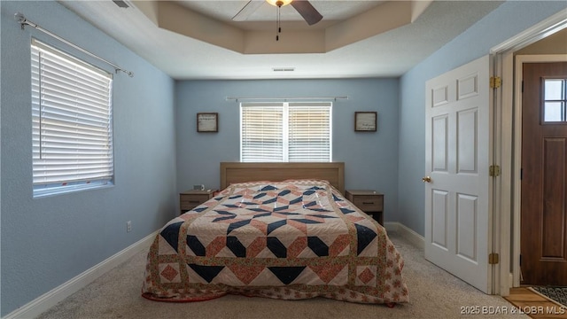 bedroom with a tray ceiling, baseboards, light colored carpet, and ceiling fan