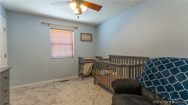 bedroom featuring a ceiling fan, a crib, light colored carpet, and baseboards