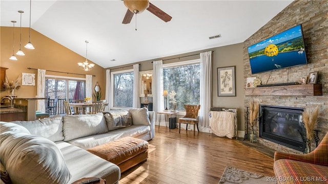 living area featuring visible vents, high vaulted ceiling, ceiling fan with notable chandelier, wood finished floors, and a stone fireplace