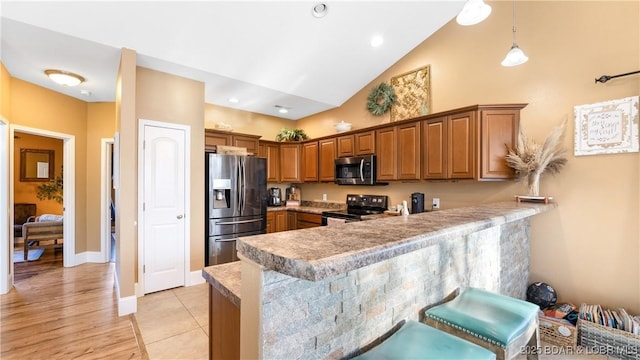 kitchen featuring a peninsula, stainless steel appliances, light countertops, a kitchen breakfast bar, and brown cabinets