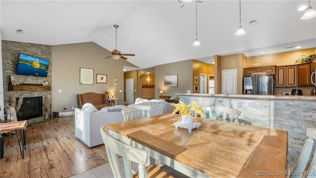 dining area featuring high vaulted ceiling, a ceiling fan, arched walkways, light wood-style floors, and a fireplace