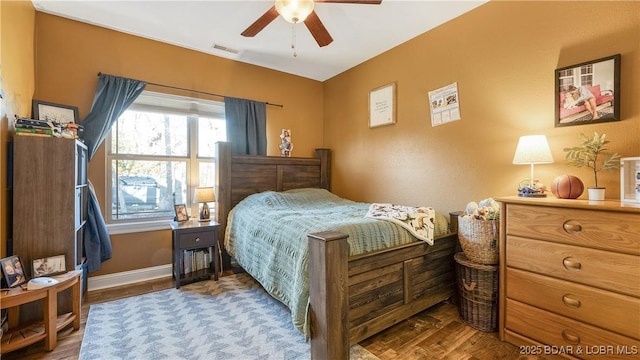 bedroom featuring ceiling fan, visible vents, baseboards, and wood finished floors