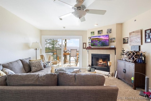 living area with light carpet, a warm lit fireplace, and a ceiling fan