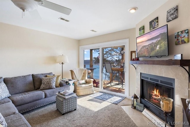 living room with a tiled fireplace, visible vents, ceiling fan, and carpet