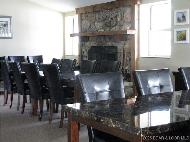 dining room featuring a stone fireplace and carpet floors