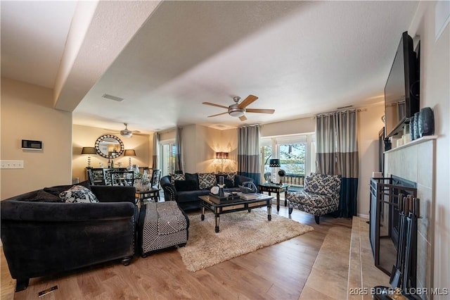 living room with ceiling fan, visible vents, wood finished floors, and a fireplace