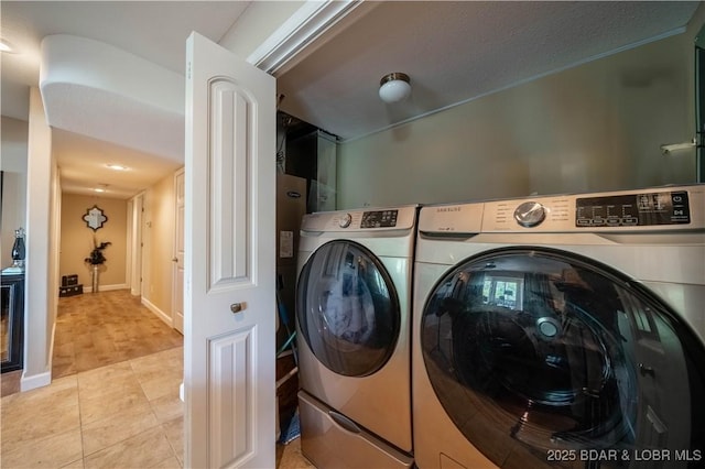 clothes washing area featuring light tile patterned flooring, laundry area, independent washer and dryer, and baseboards