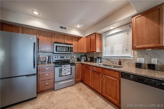 kitchen with visible vents, stone counters, brown cabinets, appliances with stainless steel finishes, and a sink