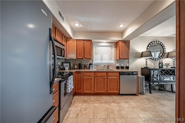 kitchen with visible vents, a sink, backsplash, appliances with stainless steel finishes, and brown cabinetry