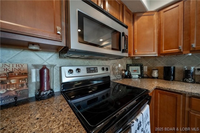 kitchen with stainless steel appliances, brown cabinets, tasteful backsplash, and light stone countertops