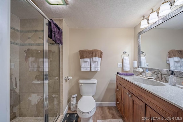 full bath with toilet, a stall shower, a textured ceiling, wood finished floors, and vanity