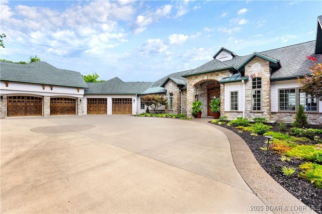 french country home with concrete driveway, an attached garage, and stone siding