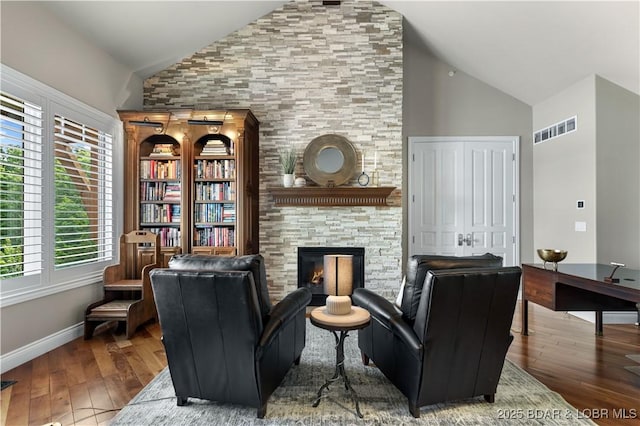 sitting room with a fireplace, visible vents, wood-type flooring, and high vaulted ceiling