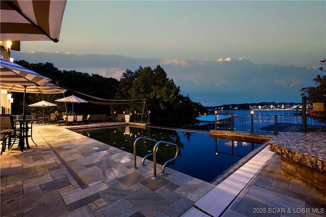 pool at dusk with a patio and a water view