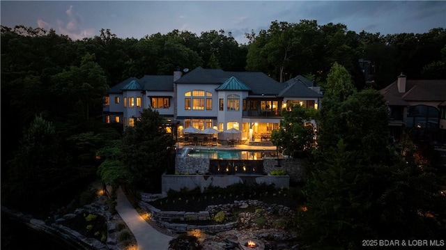 rear view of property featuring a patio area, an outdoor pool, and a chimney