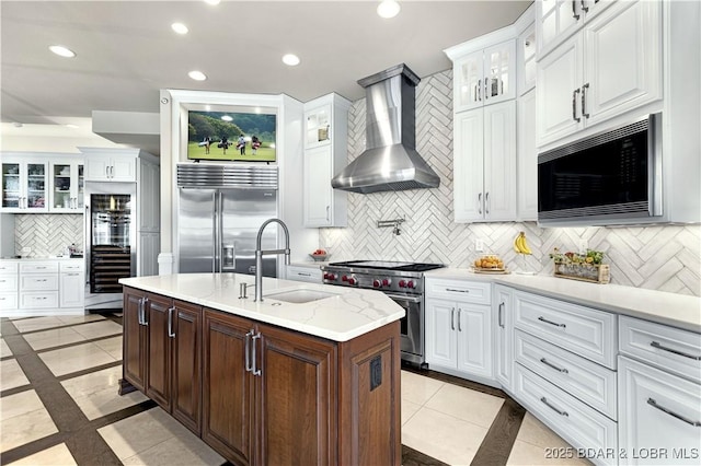 kitchen featuring recessed lighting, a sink, built in appliances, white cabinetry, and wall chimney range hood