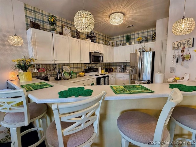 kitchen featuring a breakfast bar area, wallpapered walls, stainless steel appliances, and a peninsula