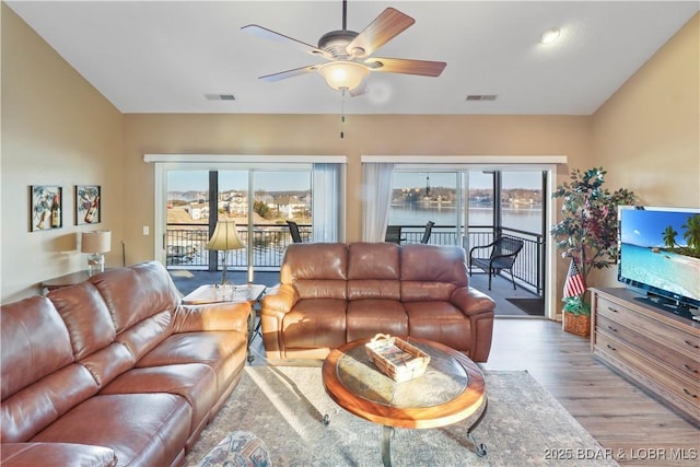 living area featuring a wealth of natural light, visible vents, wood finished floors, and a ceiling fan