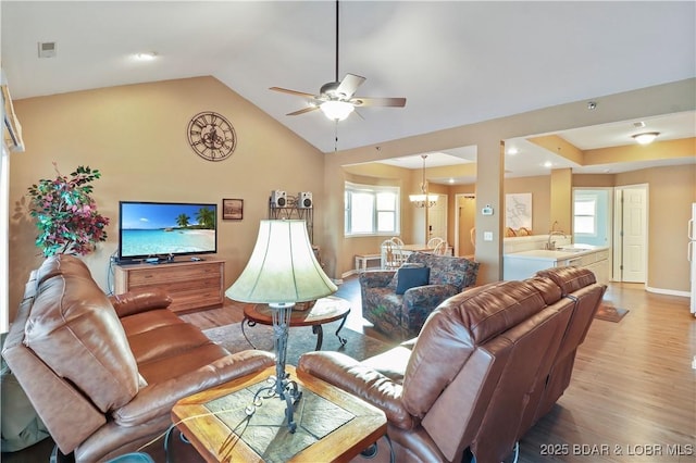 living area featuring ceiling fan with notable chandelier, lofted ceiling, light wood-style floors, and baseboards