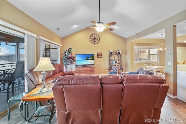 living area with a wealth of natural light, vaulted ceiling, ceiling fan with notable chandelier, and wood finished floors