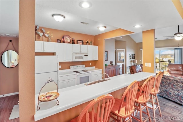 kitchen with visible vents, a sink, wood finished floors, white appliances, and a breakfast bar area