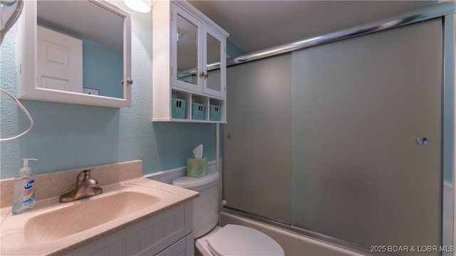 bathroom with enclosed tub / shower combo, toilet, vanity, and a textured wall