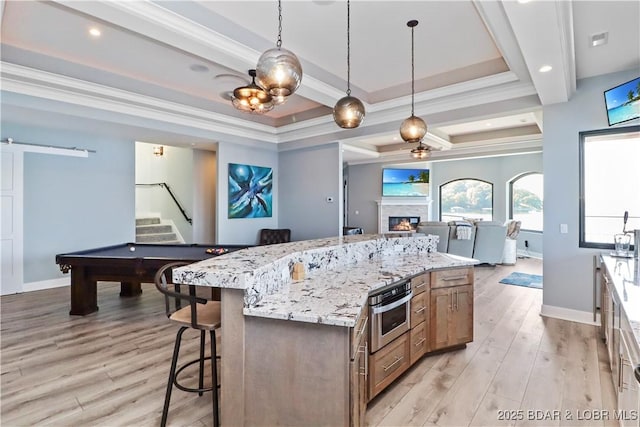 kitchen featuring a breakfast bar area, a barn door, ornamental molding, light wood-style floors, and a glass covered fireplace