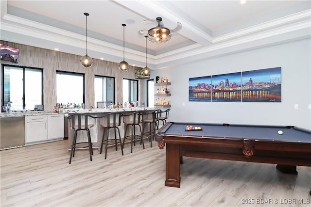 recreation room featuring a tray ceiling, wet bar, light wood-style flooring, and crown molding