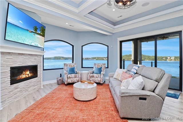 living room featuring a stone fireplace, wood finished floors, baseboards, and a water view