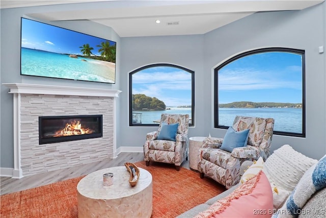 living area with a stone fireplace, visible vents, wood finished floors, and baseboards