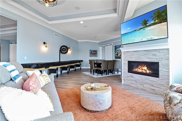 living area with wood finished floors, baseboards, visible vents, a fireplace, and ornamental molding