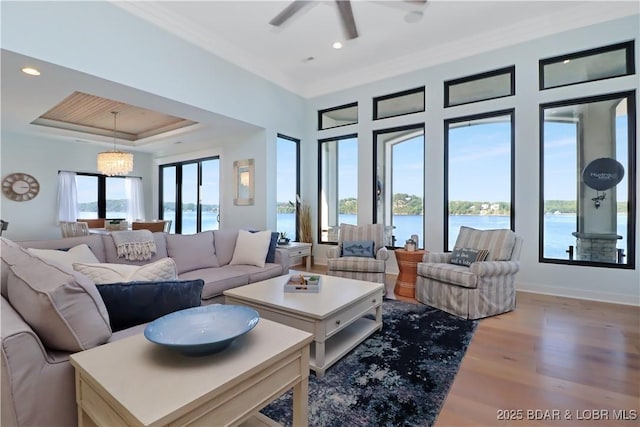 living area with a tray ceiling, a water view, wood finished floors, and ornamental molding