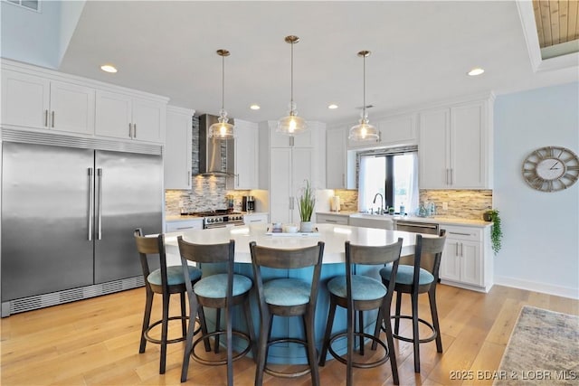 kitchen featuring light countertops, a kitchen breakfast bar, high end appliances, white cabinets, and wall chimney exhaust hood