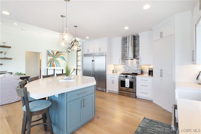 kitchen featuring wall chimney range hood, high end appliances, light wood-style flooring, and white cabinets