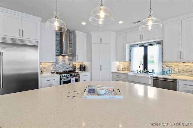 kitchen featuring visible vents, a sink, white cabinetry, wall chimney range hood, and high quality appliances