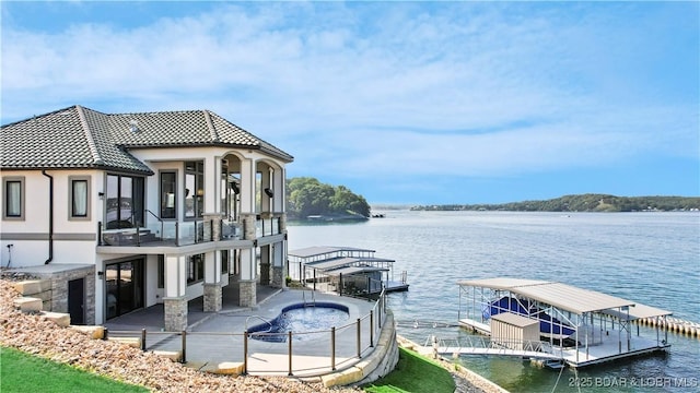 dock area with a balcony, a patio area, a water view, and a hot tub