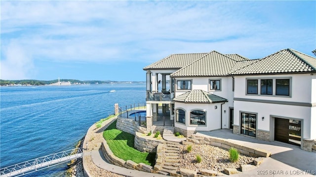 view of front of property featuring a tile roof, a garage, a water view, and stucco siding