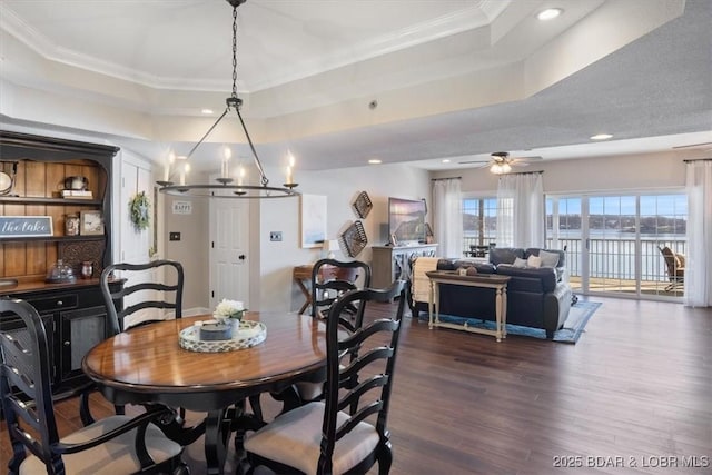 dining space featuring ornamental molding, recessed lighting, ceiling fan with notable chandelier, a raised ceiling, and dark wood-style flooring