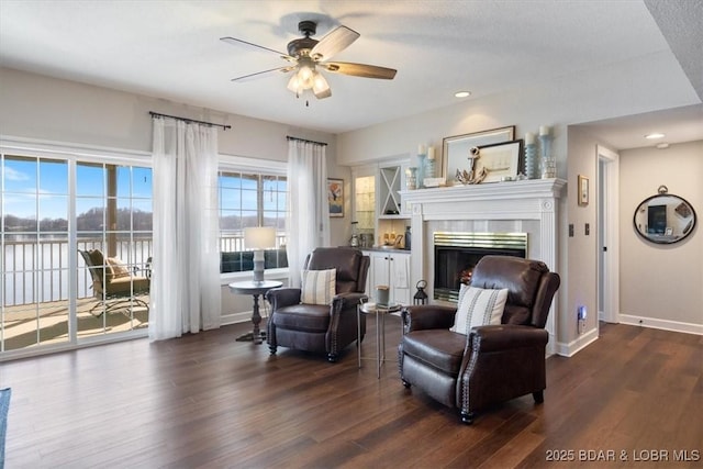 living area featuring a ceiling fan, dark wood-type flooring, a fireplace, and baseboards