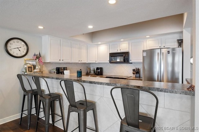 kitchen featuring dark countertops, a peninsula, black microwave, and freestanding refrigerator