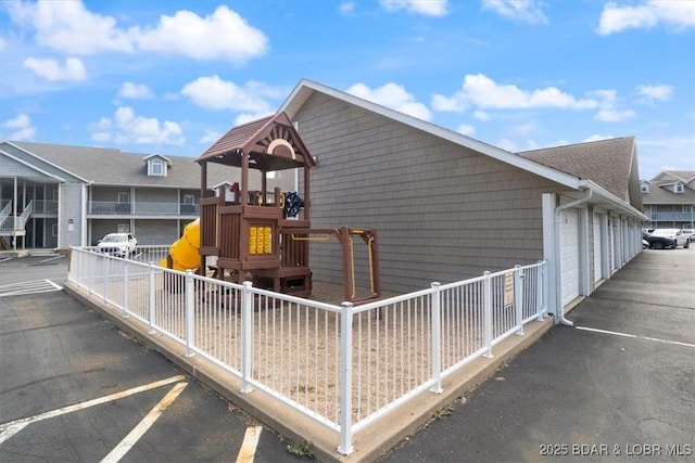 view of side of home with community garages, playground community, and fence