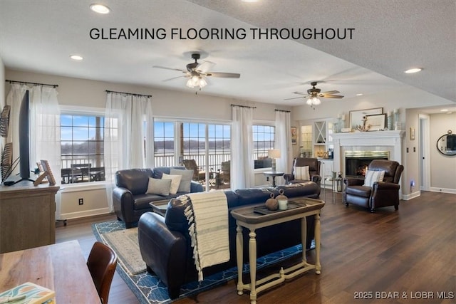 living area with baseboards, dark wood-type flooring, a lit fireplace, and a ceiling fan