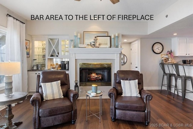 sitting room with a tiled fireplace, wood finished floors, baseboards, and ceiling fan