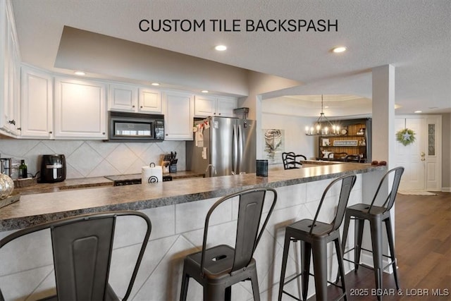 kitchen with dark countertops, white cabinetry, freestanding refrigerator, a peninsula, and black microwave