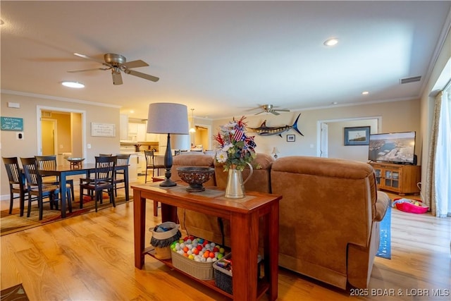 living room with crown molding, a ceiling fan, and light wood finished floors