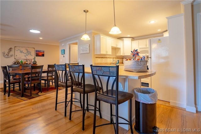 kitchen with a breakfast bar area, freestanding refrigerator, ornamental molding, light countertops, and light wood-type flooring