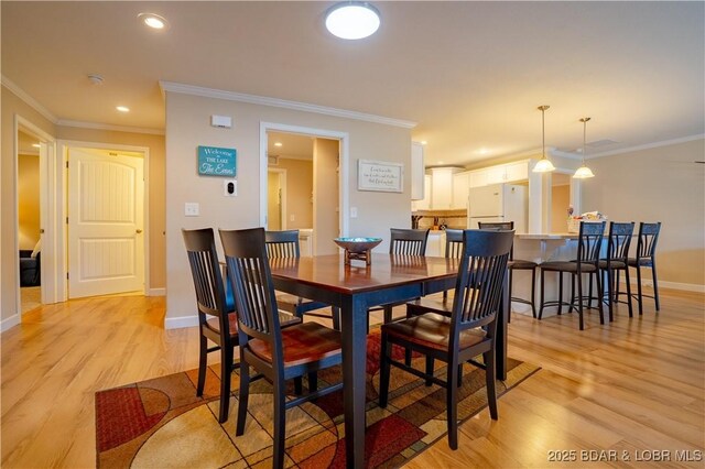 dining room featuring light wood-type flooring, baseboards, and ornamental molding