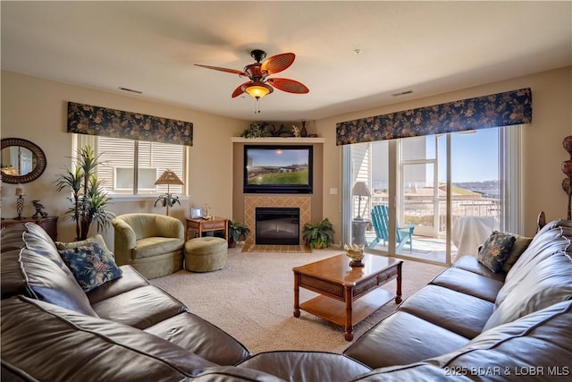 carpeted living area with a tiled fireplace, a ceiling fan, and visible vents