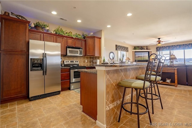 kitchen with visible vents, backsplash, open floor plan, appliances with stainless steel finishes, and a breakfast bar area