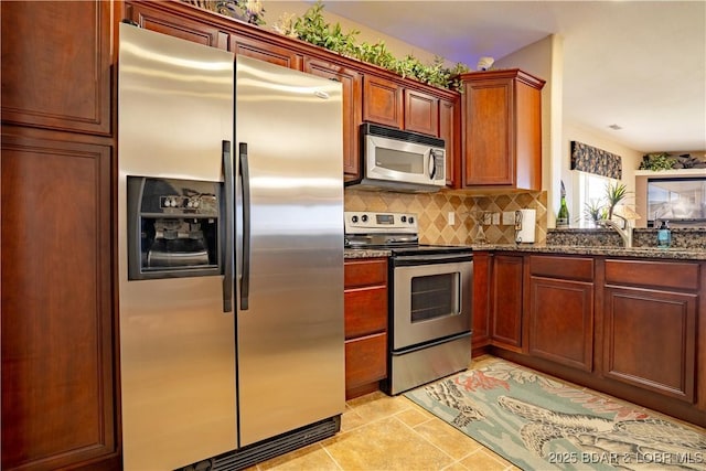 kitchen with dark stone countertops, a sink, tasteful backsplash, appliances with stainless steel finishes, and light tile patterned floors